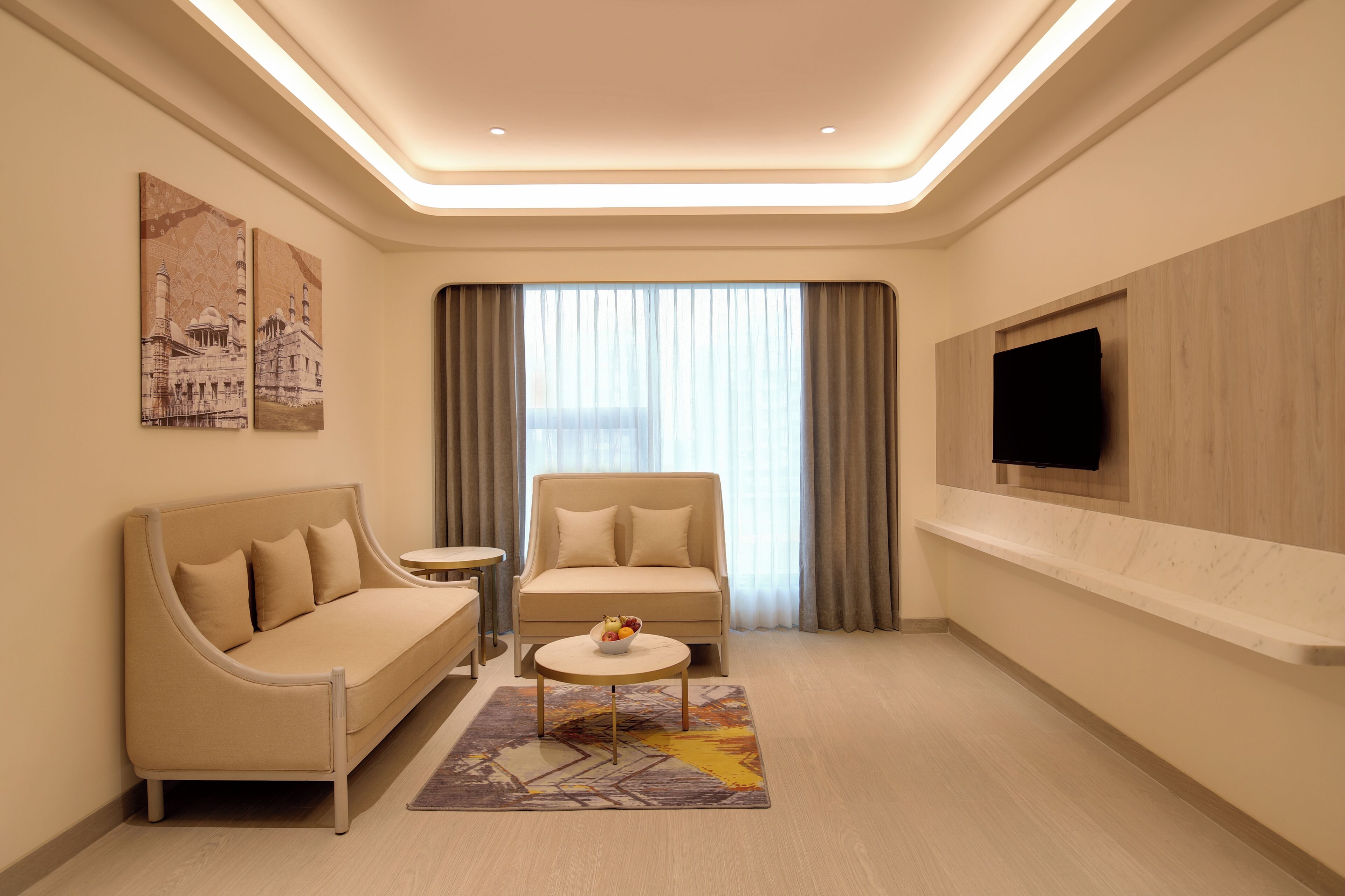 Une chambre d’hôtel moderne, équipée d’un canapé, d’un fauteuil, d’une petite table et d’un téléviseur fixé au mur.