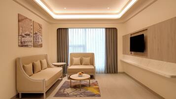 Ein modernes Hotelzimmer mit Sofa, Sessel, kleinem Tisch und einem an der Wand befestigten Fernseher.
