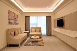 Una habitación de hotel moderna con un sofá, una silla, una mesita y un televisor montado en la pared.