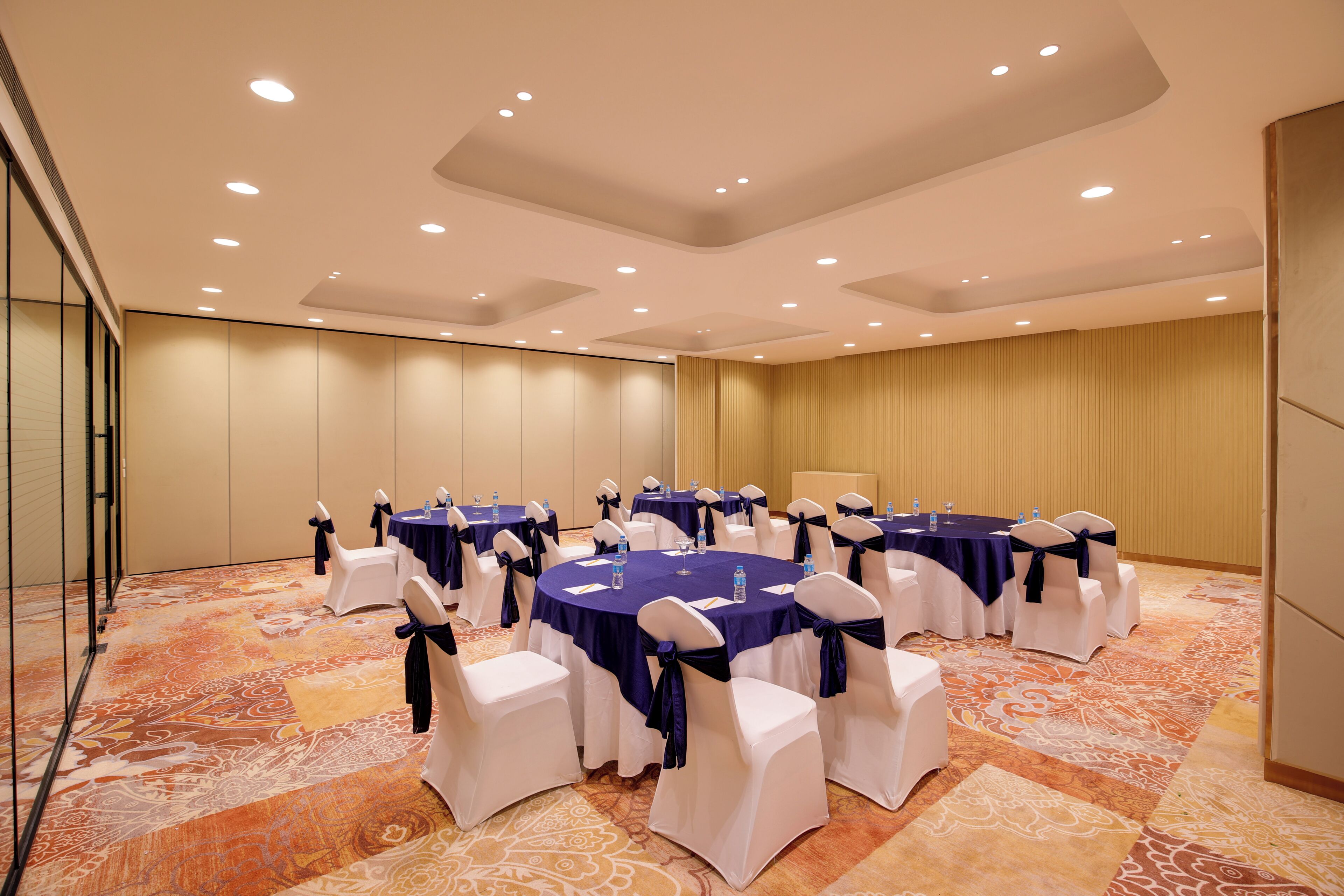 A conference room with round tables, white chairs, and blue tablecloths.