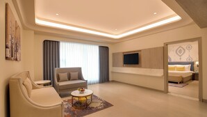 A modern hotel room with a sofa, armchair, small table, and a TV mounted on the wall. -  Lemon Tree Hotel, Bharuch (Bharuch)