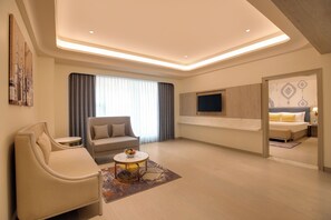 A modern hotel room with a sofa, armchair, small table, and a TV mounted on the wall. -  Lemon Tree Hotel, Bharuch (Bharuch)