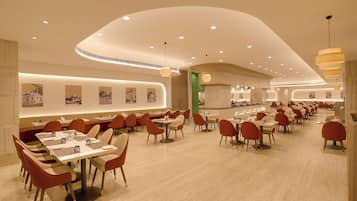 A spacious restaurant with multiple dining tables and chairs, a curved ceiling design, and wall-mounted artwork.