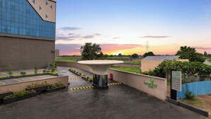 A hotel entrance with a modern building, a water feature, and a sunset in the background. -  Lemon Tree Hotel, Bharuch (Bharuch)