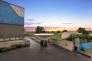A hotel entrance with a modern building, a water feature, and a sunset in the background. -  Lemon Tree Hotel, Bharuch (Bharuch)