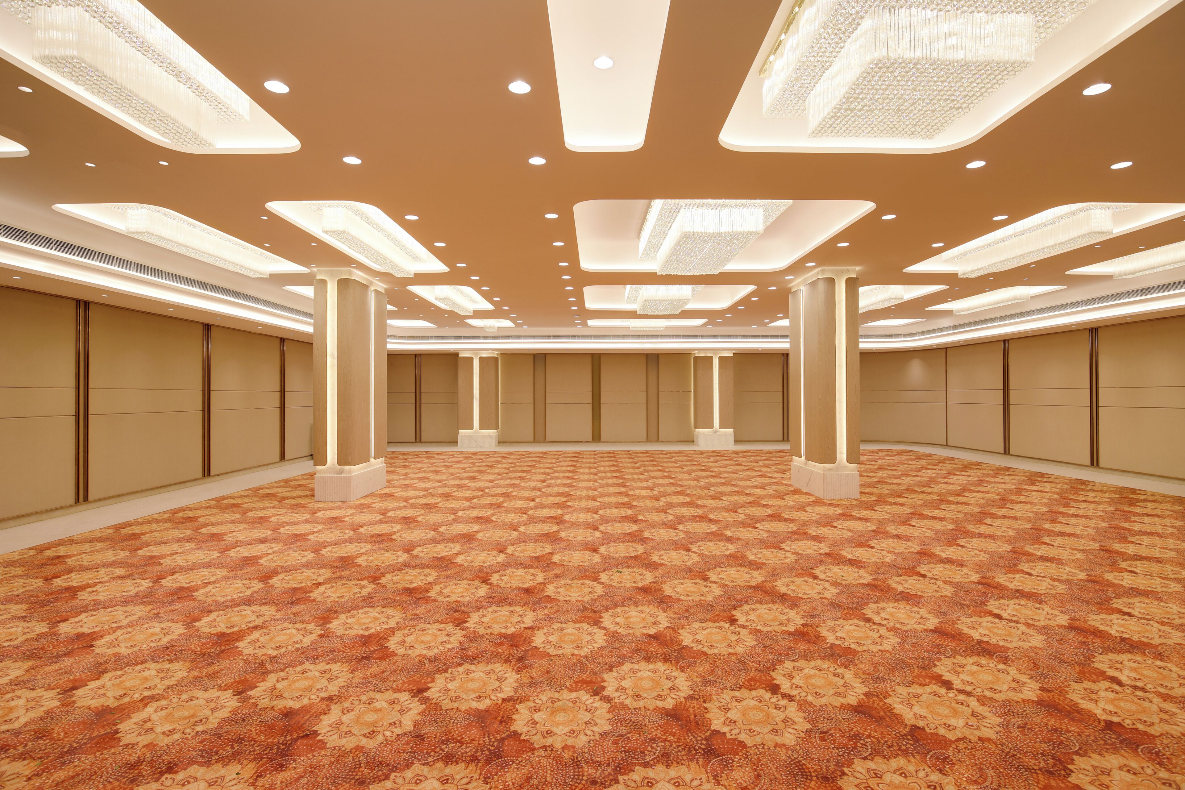 A spacious room with a patterned carpet, recessed lighting, and a symmetrical layout with columns.