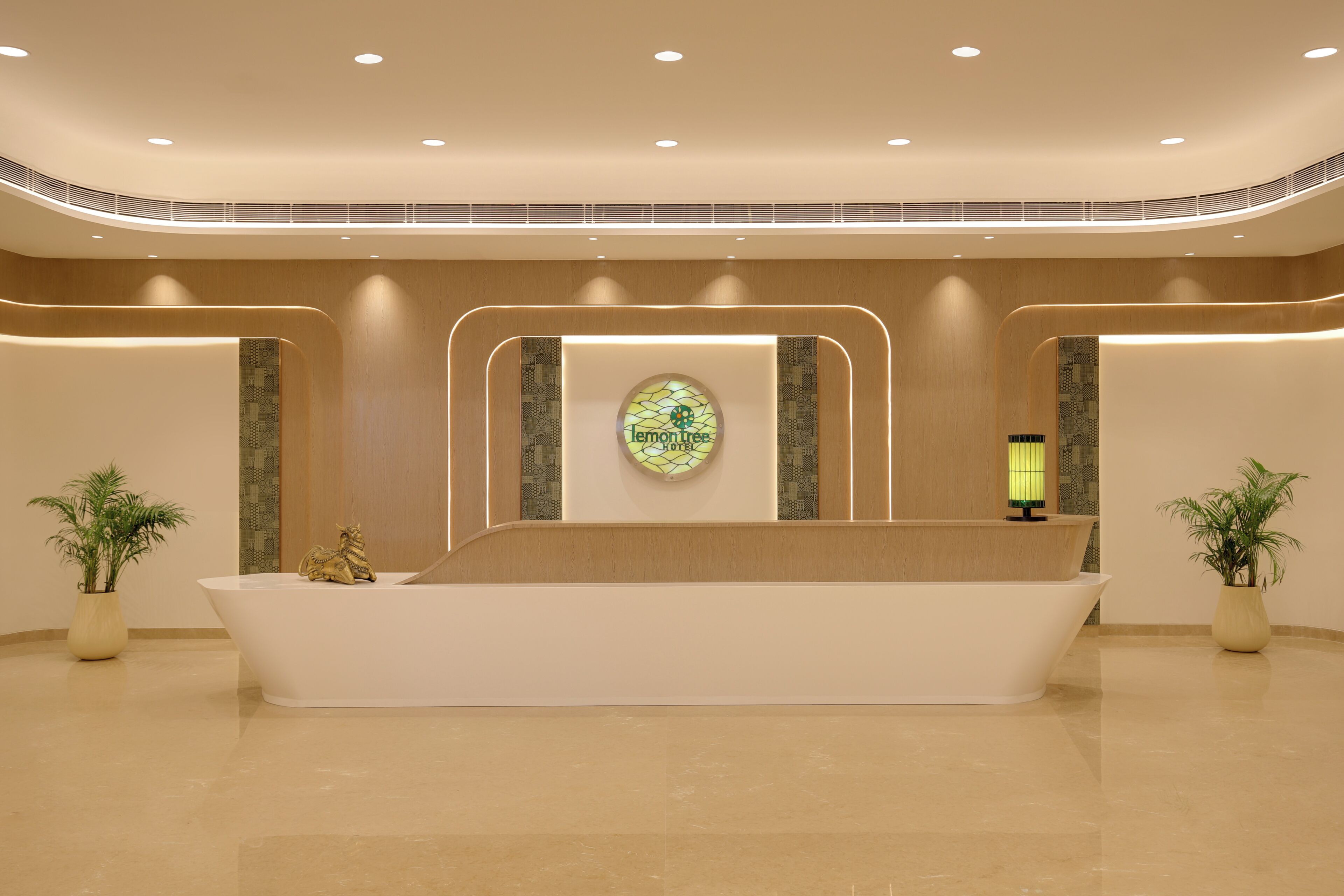 Un mostrador de recepción con un emblema circular, dos plantas en macetas y una pared con diseño.