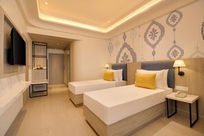 Habitación de hotel con dos camas, un televisor, una mesita de noche con lámpara y una pared con diseño decorativo.