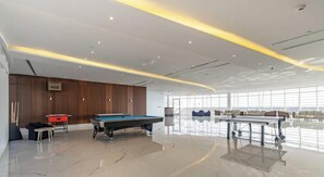A modern indoor pool area with a pool table, lounge chairs, and a wooden wall. - Peaceful Studio | Opalz by Danube | BMS (Dubai)