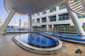 Ein modernes Gebäude mit Poolanlage, darunter ein runder Pool und ein rechteckiger Pool, umgeben von einer weißen Brüstung.