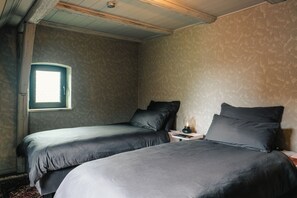 Ein Zimmer mit zwei Betten, einem kleinen Nachttisch mit Lampe und einem Fenster.