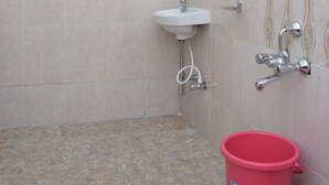 Une salle de bain avec une douche, un lavabo et un seau rouge.