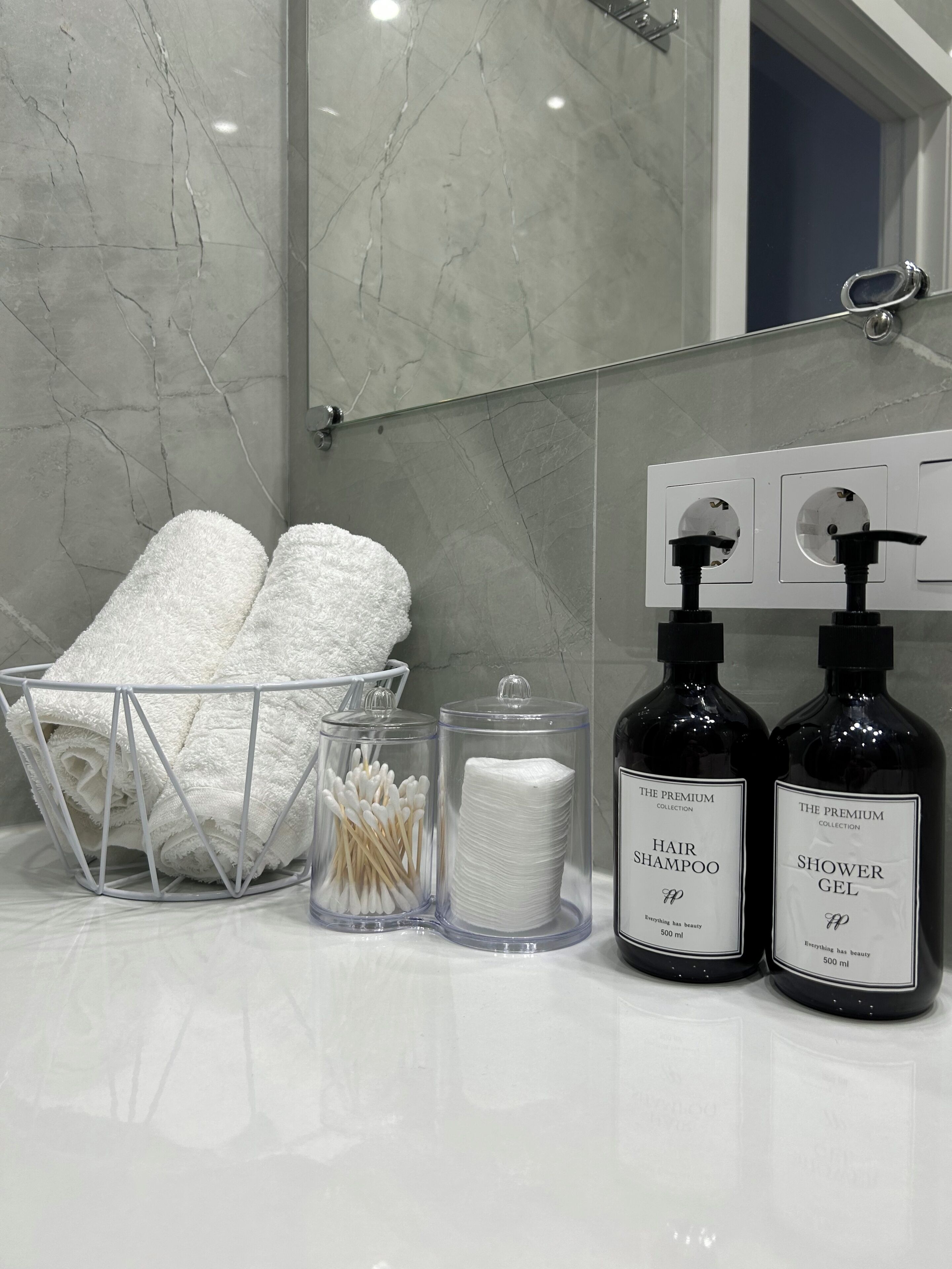 Ein Badezimmer-Waschtisch mit Marmor-Spritzschutz, ein Handtuchhalter mit gefalteten Handtüchern, eine Dose Wattestäbchen und zwei Flaschen Haarspray und Duschgel.