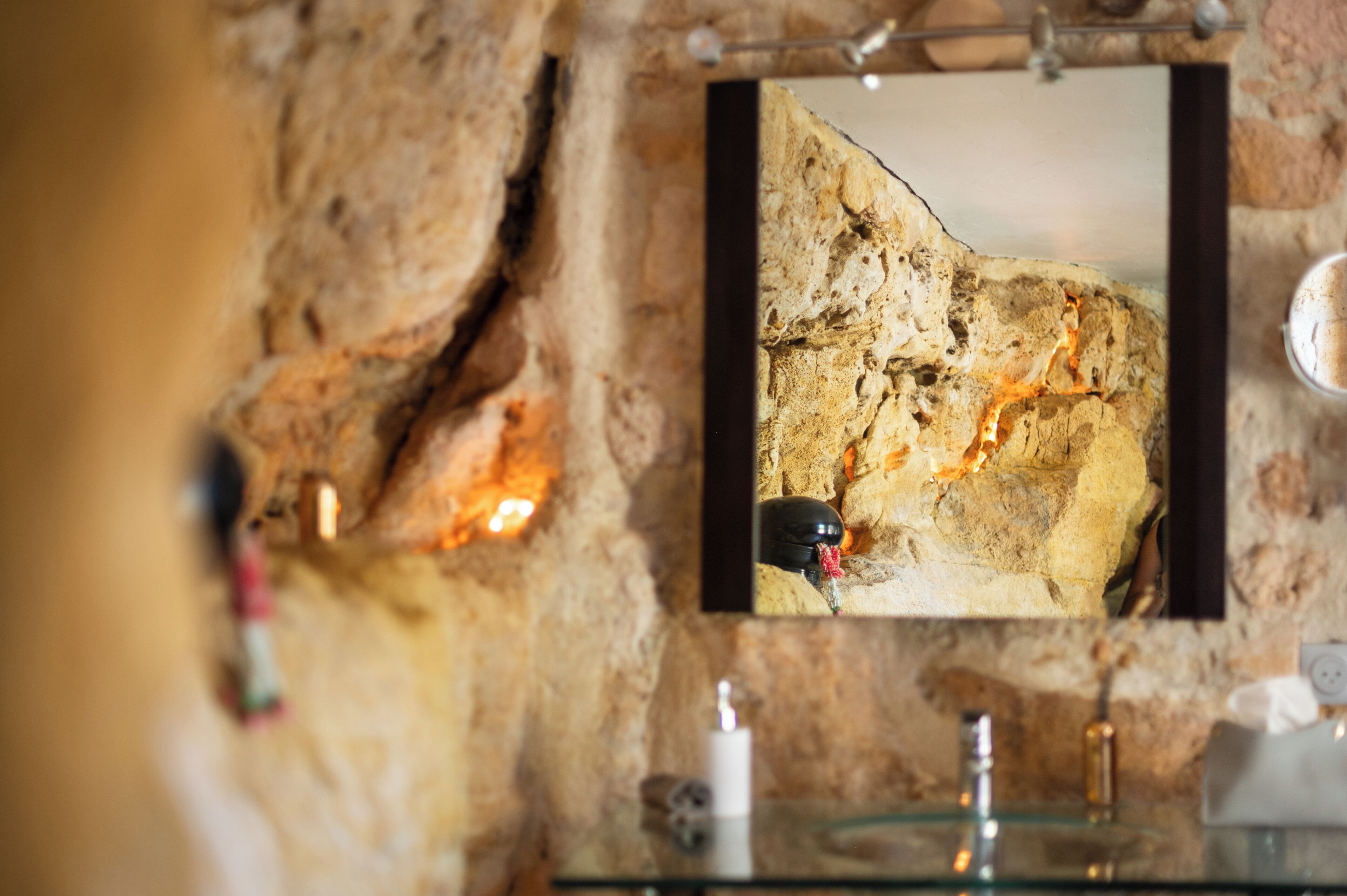 A bathroom with a stone wall, a mirror, and a glass sink.