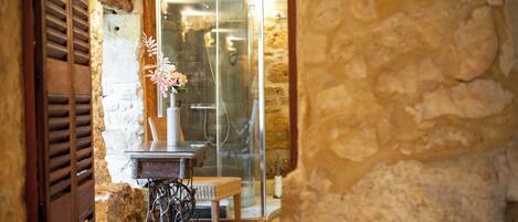 Un muro de piedra, una mesa de madera con un florero, y una silla de mimbre en una habitación con puerta de cristal.