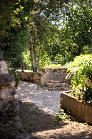 Un jardin avec un mur de pierre, une clôture en bois et des chaises en osier.