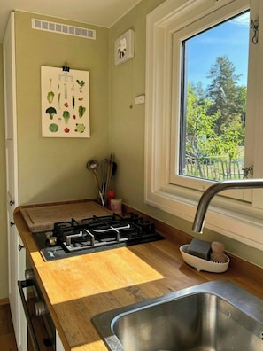 A kitchen with a gas stove, wooden countertop, stainless steel sink, and a window with a view of greenery.