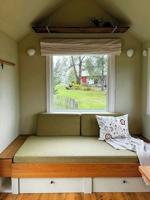 A cozy room with a built-in bench seating area, a window with a checkered valance, and a view of a garden.