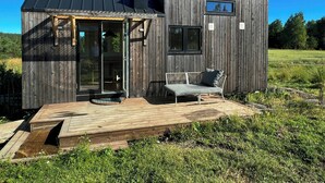 Pieni puinen mökki, jossa on terassi, penkki ja ikkuna.