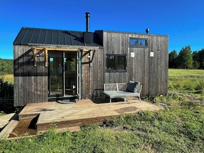 Eine kleine Holzhütte mit einer Terrasse, einer Bank und einem Fenster.