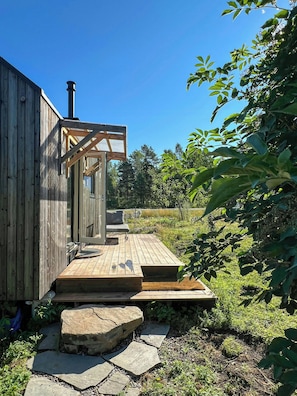 A wooden cabin with a deck, a chimney, and a stone pathway leading to a bench.