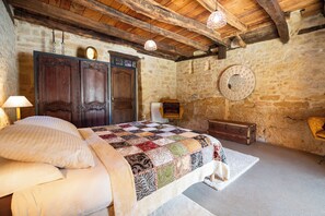 A bedroom with a wooden bed, a stone wall, a wooden ceiling, and a round mirror. - Troglodyte Cottage with Private Pool near Sarlat (Vitrac)