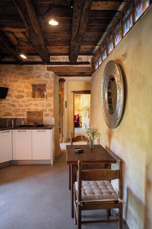 A rustic interior with stone walls, wooden beams, a dining table with chairs, and a large mirror on the wall. - Troglodyte Cottage with Private Pool near Sarlat (Vitrac)
