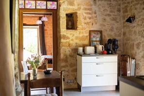 Quarto com parede de pedra, cómoda branca, mesa com um vaso e cadeira de madeira.