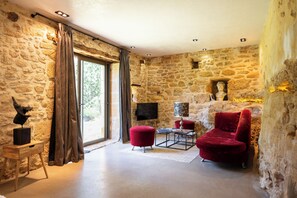 A stone-walled room with a red chair, a small table, and a flat-screen TV mounted on the wall. - Troglodyte Cottage with Private Pool near Sarlat (Vitrac)