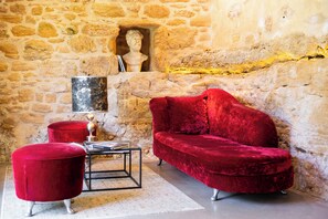 A room with a stone wall, a red velvet sofa, a matching ottoman, and a small table with a book. - Troglodyte Cottage with Private Pool near Sarlat (Vitrac)