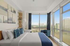 A modern hotel room with a large bed, a seating area, and a view of the cityscape through large windows. - Ravora by Kozystay - Sungkono (Surabaya)