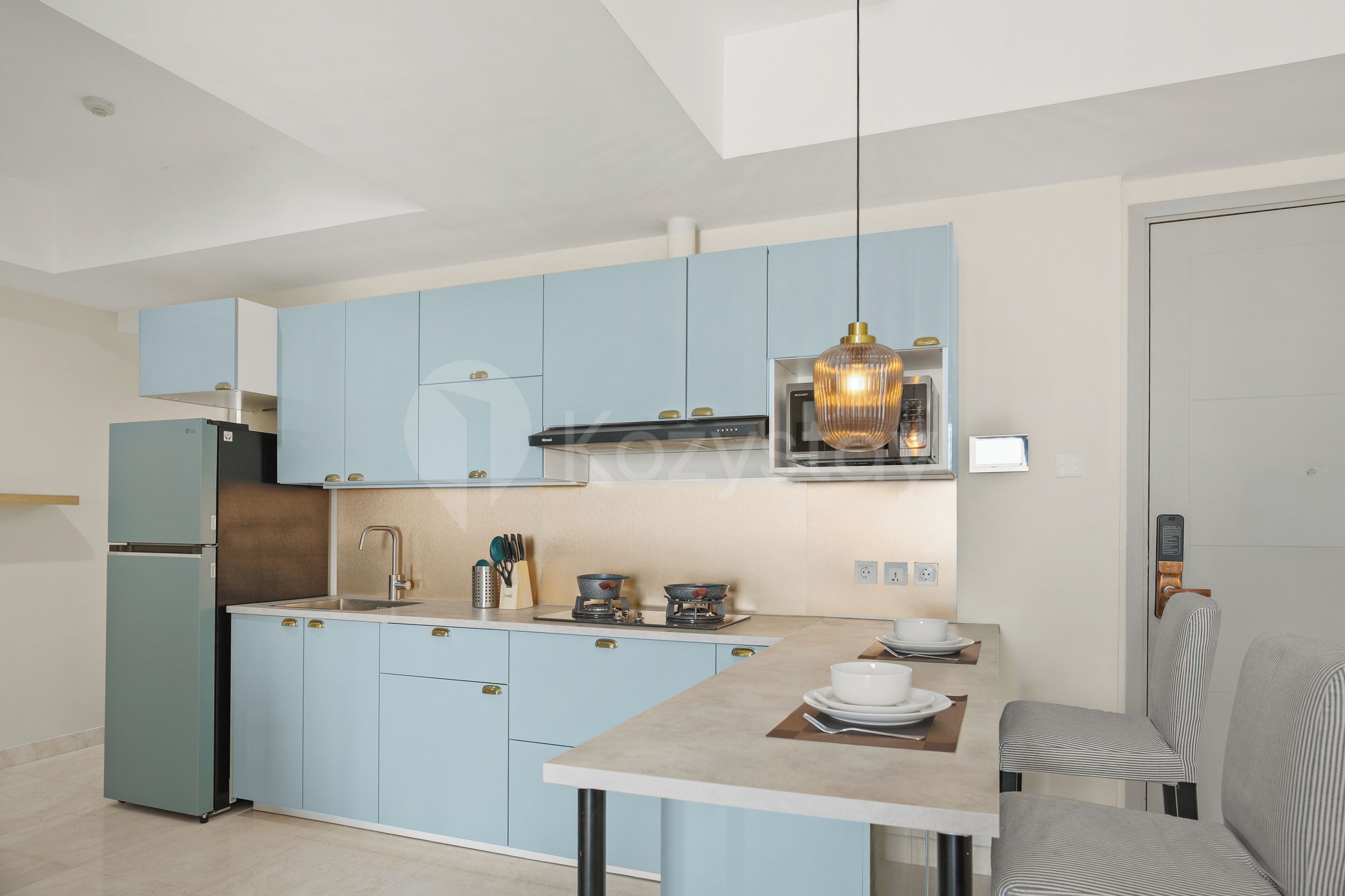 Eine moderne Küche mit hellblauen Schränken, einem Edelstahlkühlschrank, einem Gasherd und einer hängenden Pendelleuchte.