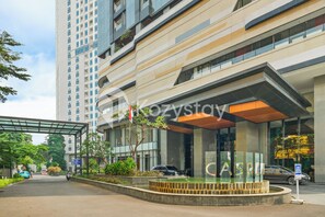 A modern building with a covered entrance, a parking area, and a tall residential building in the background. - Ravora by Kozystay - Sungkono (Surabaya)