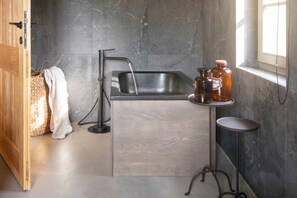 A modern kitchen with a built-in sink, a wooden cabinet, a woven basket, and a small round table with bottles. - Villa Panorama Del Tartufo (Buzet)