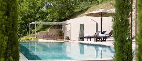 Una piscina con sillas de descanso y una pérgola, rodeada de vegetación.