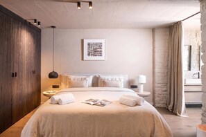 Une chambre moderne avec un grand lit, des tables de chevet, une commode, un tableau encadré au mur et un mur à la texture de pierre.