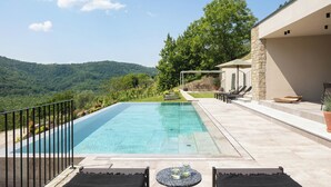 A rectangular swimming pool with a clear blue water surface, surrounded by a paved deck with lounge chairs and a table. - Villa Panorama Del Tartufo (Buzet)