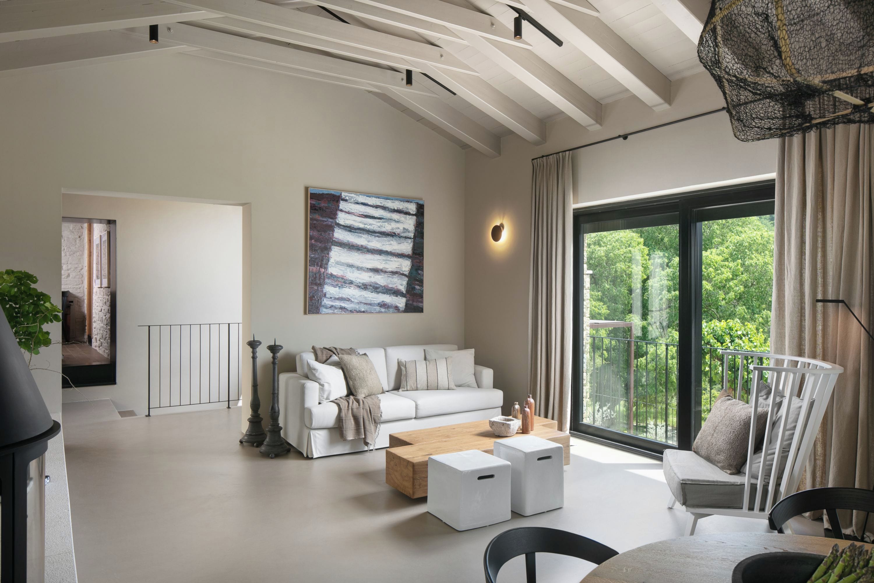 Een ruime woonkamer met een witte bank, een salontafel en een groot raam met uitzicht op groen.