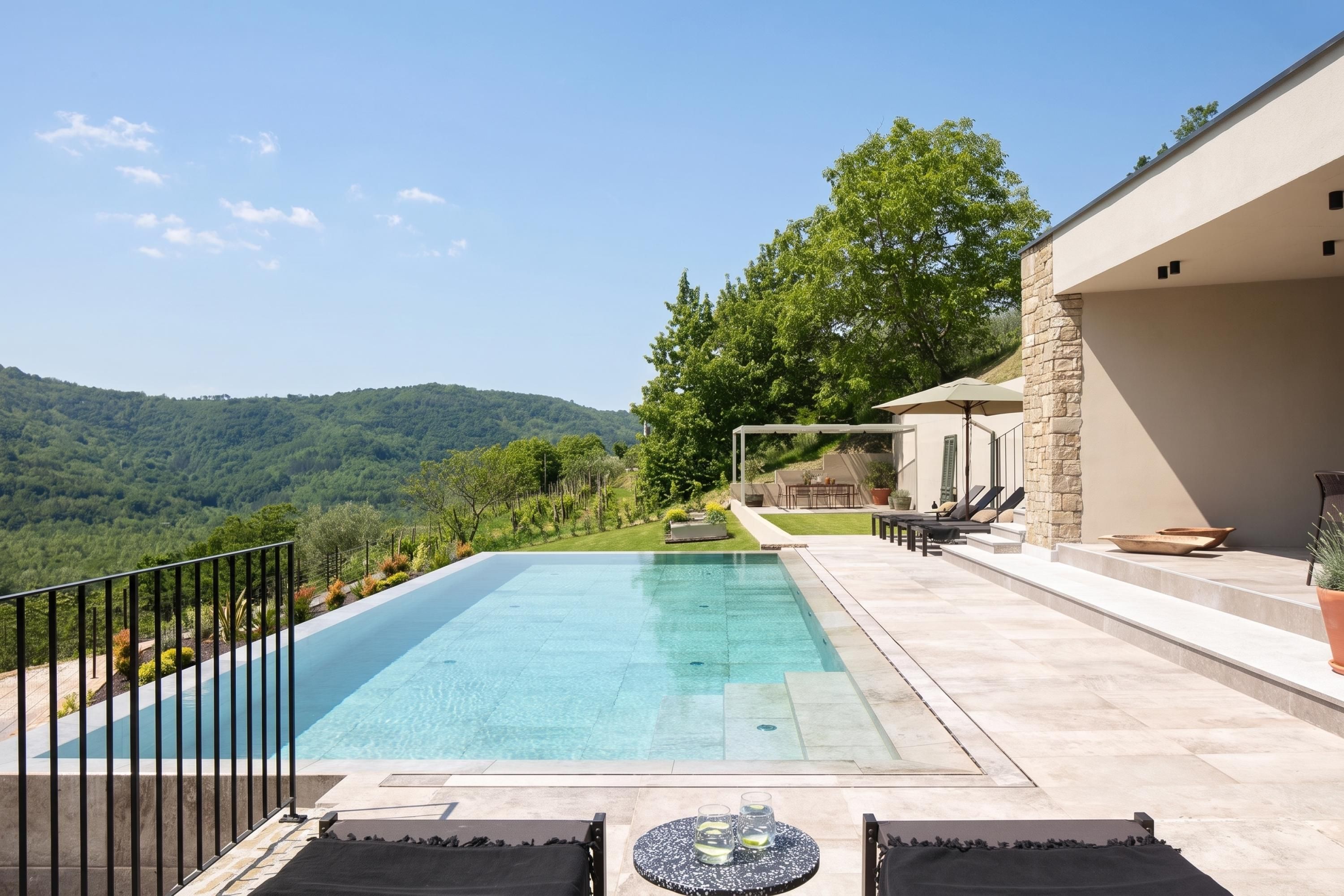 A rectangular infinity pool with clear blue water, surrounded by a stone deck and black metal railings.