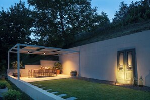 Eine moderne Terrassengruppe mit Tisch und Stühlen, umgeben von einer niedrigen Mauer und einem überdachten Sitzbereich.
