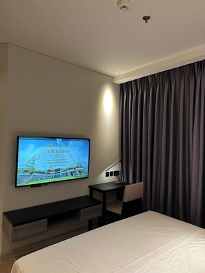 Ein Hotelzimmer mit einem Bett, einem Schreibtisch mit Stuhl, einem an der Wand befestigten Fernseher und einem Fenster mit Vorhängen.