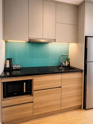 Eine moderne Küche mit Holzschränken, einer schwarzen Arbeitsplatte, einer eingebauten Mikrowelle und einem Edelstahlkühlschrank.