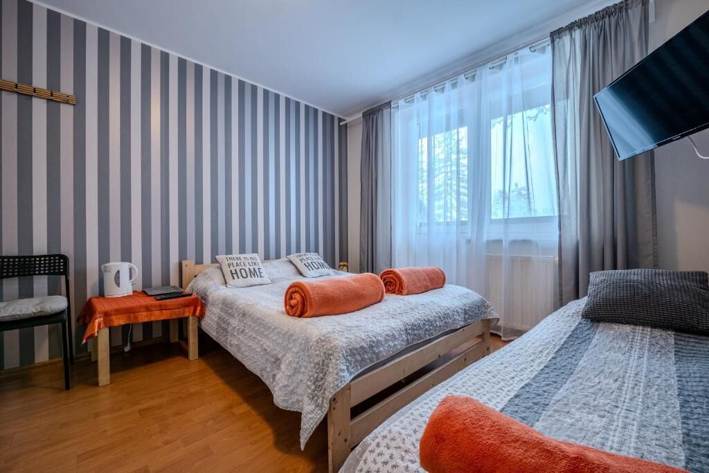 A hotel room with a bed, a chair, a small table with a kettle, and a TV mounted on the wall.