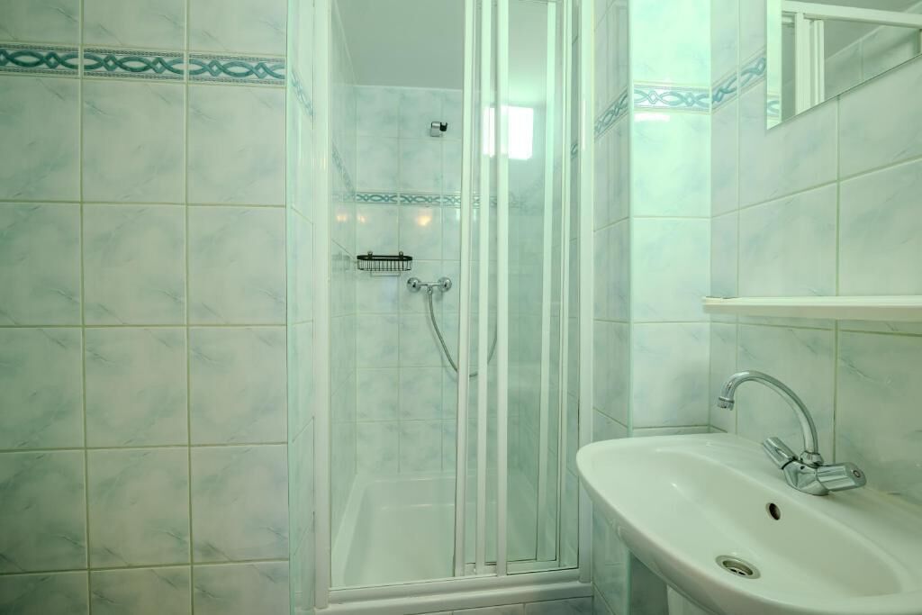 Ein Badezimmer mit einer Duschkabine, einem weißen Waschbecken und einem Spiegel darüber.