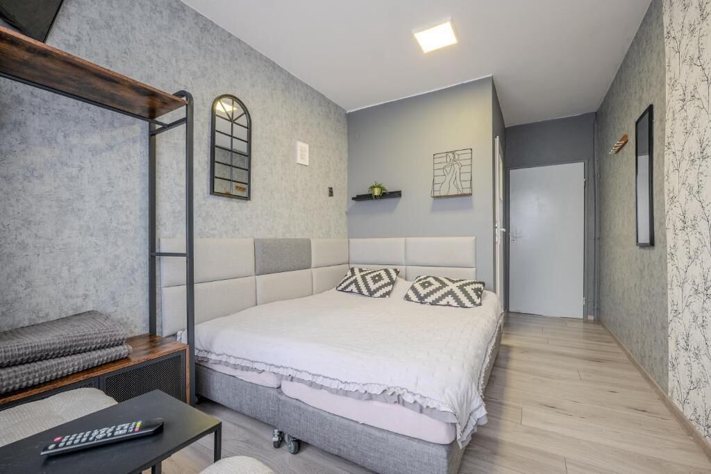 A bedroom with a bed, a bench, a small table, and a wall-mounted shelf.