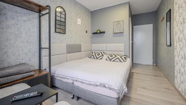 A bedroom with a bed, a bench, a small table, and a wall-mounted shelf.