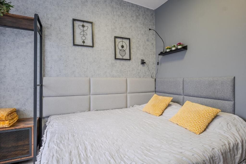 A bedroom with a bed, a headboard, a shelf with plants, and artwork on the wall.