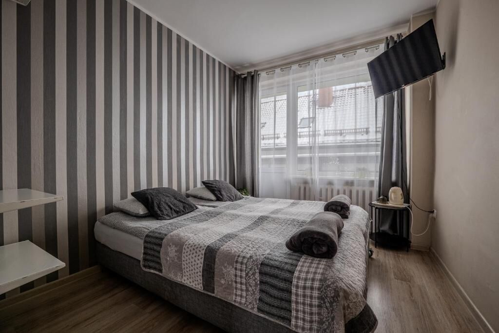 Un dormitorio moderno con cama, mesita de noche, televisor de pantalla plana y ventana con cortinas.