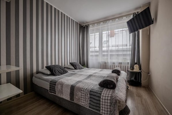 A modern bedroom with a bed, a bedside table, a flat-screen TV, and a window with curtains.