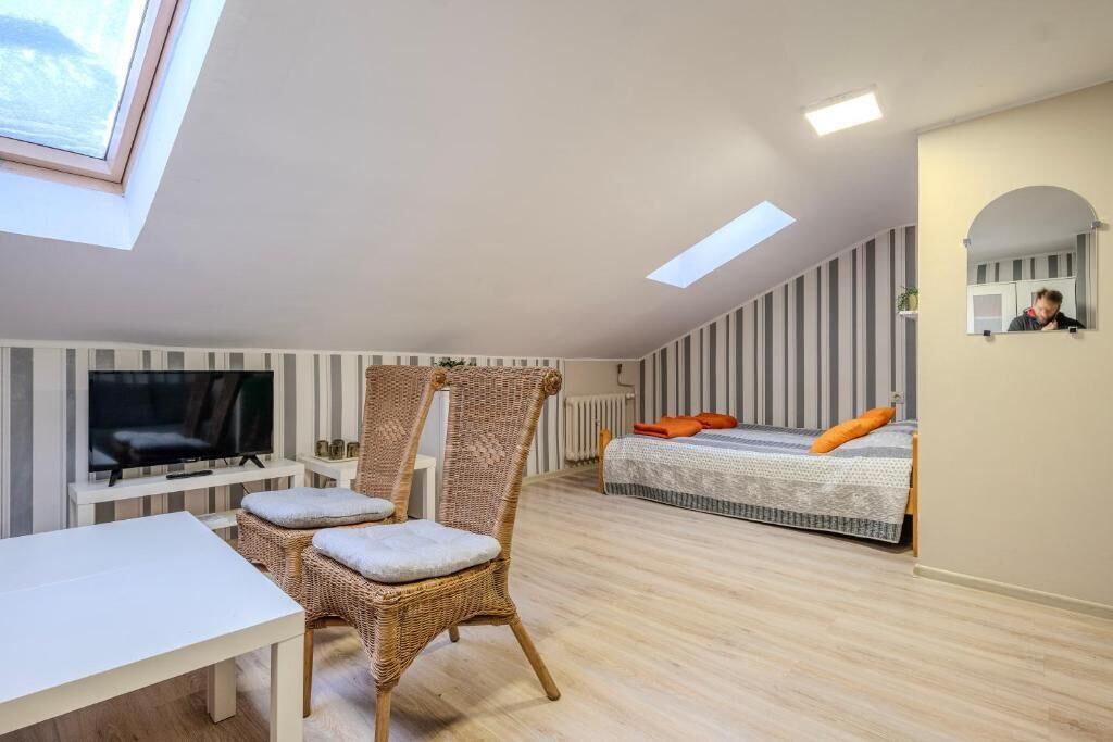 A modern bedroom with a flat-screen TV, a bed with orange pillows, a wicker chair, and a skylight.